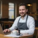 Happy restaurant owner sitting in front of his laptop making use of Zapper merchant features