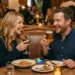 Man and a woman smiling while having dinner and drinks at a restaurant with a phone on the table showing the Zapper app home screen
