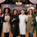 Six women professionally dressed standing arm in arm and smiling at the camera
